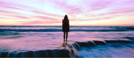 Woman in silouette contemplating sunset at ocean.